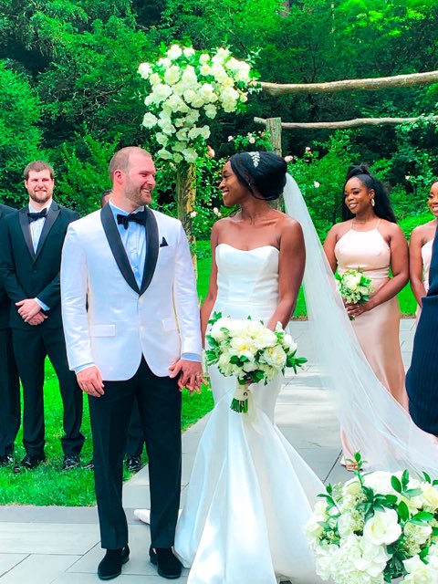 Nathan in suit and Jasmine in wedding gown, on white runner with wedding guests around them